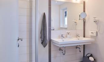 A modern bathroom with a shower, a vanity, and a large mirror. The walls are bright and the furnishings are simple and elegant.