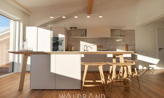 A modern kitchen with bright furniture and a large table.  

A lot of sunlight enters the room through large windows.
