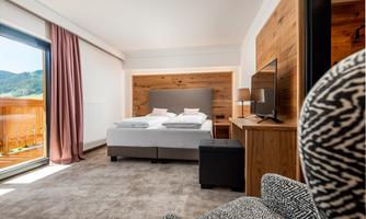 A modern hotel room with two beds and a beautiful wooden interior. A balcony offers a view of the mountains.