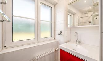 A modern bathroom with bright tiles and a sink in red design. Large windows provide plenty of daylight.
