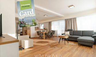 A modern living room with a sofa and a dining table. In the foreground, the Schladming-Dachstein Card is visible.