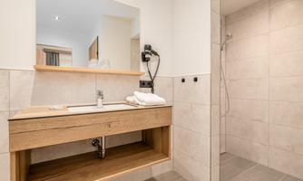 A modern bathroom with a wooden sink and a shower. The walls are brightly tiled and the furnishings are simple and functional.