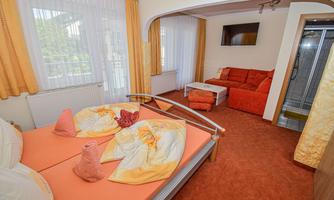 A cozy room with a double bed, orange walls, and a red sofa. There is also a TV and windows with curtains.