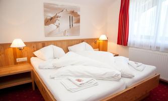 A cozy bedroom with a double bed and white bedcovers. The walls are in warm wood tones and there is soft light from the bedside lamps.