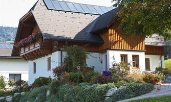 A beautiful wooden house with a planted garden. The facade is bright, surrounded by colorful flowers and greenery.
