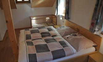 A cozy bedroom with a double bed and a children's bed. It is bright and friendly with wooden details and windows.