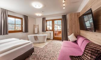 A modern room with two single beds, a cozy sofa, and a freestanding bathtub. Large windows provide plenty of natural light and a view of the landscape.