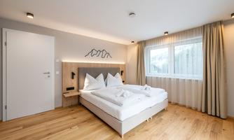 A modern bedroom with two single beds and wooden flooring. Large windows provide plenty of daylight and a cozy atmosphere.