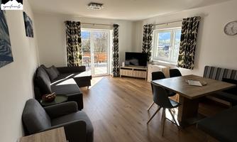 A modern living room with a cozy seating area and a dining table. Large windows provide plenty of daylight and a view outside.