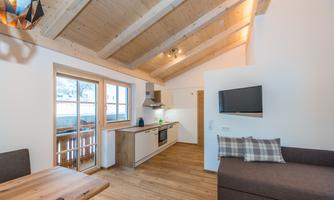 A bright, modern kitchen with a wooden ceiling and a cozy living area. Large windows provide plenty of daylight and an inviting atmosphere.