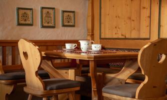 A cozy wooden table with two cups and a decorative tablecloth. Around the table, there are chairs with heart-shaped cutouts.