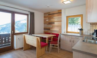 A cozy kitchen and dining area with wooden details and red chairs. Large windows offer a beautiful view of the landscape.