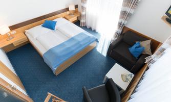 A modern hotel room with a large double bed and a cozy seating area. The room is bright and tastefully furnished, with plenty of natural lighting.