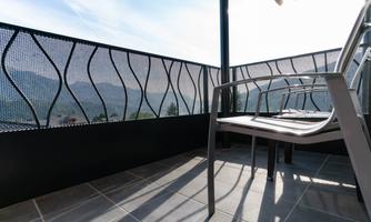 A balcony with a modern railing and a chair. In the background, gentle hills and a blue sky can be seen.