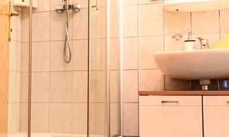 A modern bathroom with a shower and a sink. The floor is tiled and a yellow towel is lying on the floor.