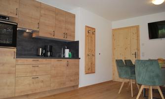 A cozy kitchen with wooden cabinets and modern appliances. The dining area consists of a table and chairs in soft colors.