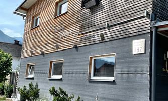 A modern house with wooden cladding and large windows. The entrance area is designed with plants and decorative elements.