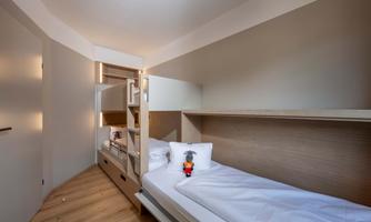 A modern room with two beds and wooden shelves. A stuffed animal is lying on one of the beds.