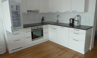 A modern kitchen with white cabinets and a wooden countertop. It includes a refrigerator, a stove, and a coffee machine.