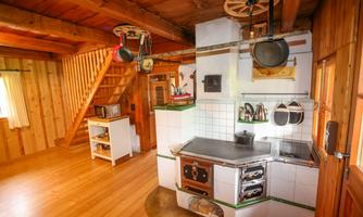 A rustic kitchen with wooden paneling and a traditional stove. In the background, stairs and additional kitchen elements are visible.