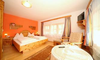 A cozy room with a large bed and warm wood colors. There is a seating area and a television, while the window lets in plenty of natural light.