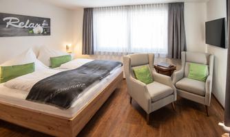 A modern bedroom with a large bed and two cozy armchairs. Bright curtains and a relaxing ambiance create an inviting atmosphere.