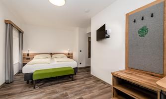 A modern bedroom with a double bed and wooden floor. The walls are light-colored, and there is a cozy sitting area with a television.