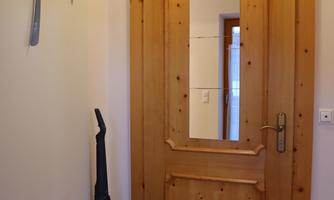An entrance area with a wooden door and a mirror. There are coat hooks hanging on the wall, and a vacuum cleaner stands next to the door.