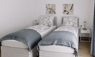 A cozy bedroom with two single beds and a bright, modern design. The walls are adorned with stylish artworks.