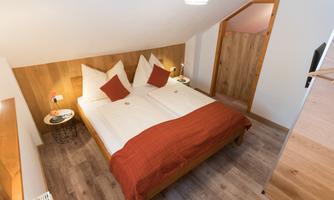 A cozy bedroom with a double bed and wooden paneling. The white cushions and the red bedspread create an inviting atmosphere.