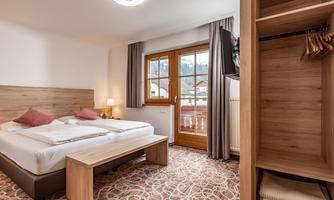A modern bedroom with a double bed and a cozy sitting area. Through the window, you can see the mountains and plenty of daylight streams in.