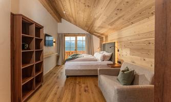 A modern room with a wooden ceiling and large windows. It has a double bed, a seating area, and a cozy atmosphere.