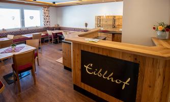 A cozy restaurant with a wooden counter and tablecloths. The seating areas are designed to be friendly and inviting.