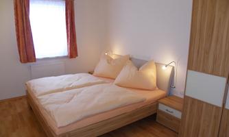 A cozy bedroom with a double bed and two large pillows. The room has light walls and a window that lets in natural light.
