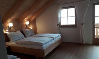 A cozy bedroom with wooden ceilings and two beds. There is a window area with curtains and a beautiful view.