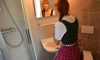 A person in traditional costume washes their hands in front of a mirror. The room is brightly and modernly designed.