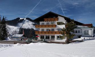 A cozy building in a winter landscape with snow. In the background, there are mountains and a clear blue sky.