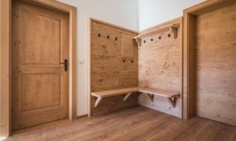 A modern hallway with wooden paneling and a bench. The walls are equipped with coat hooks.