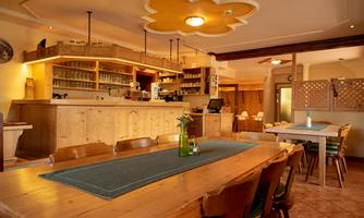 A cozy dining area with wooden shelves and a bar. Tables are neatly set, and the lighting creates an inviting atmosphere.