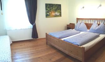 A cozy room with a double bed and a table. The wooden floor and natural lighting create a relaxed atmosphere.