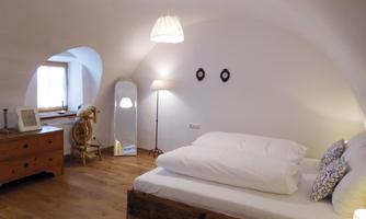 A cozy bedroom with a wooden bed and white bedding. The room has a bright, inviting look with a large mirror and a desk.