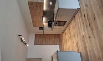 A modern kitchen with wood and gray elements. It features a stove, a sink, and a microwave.