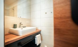 A modern bathroom with a stylish sink and wooden shelves. The walls are brightly tiled, creating a cozy atmosphere.