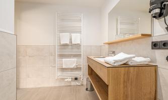 A modern bathroom with a wooden sink and fresh towels. Bright tiles and a large mirror create an inviting atmosphere.
