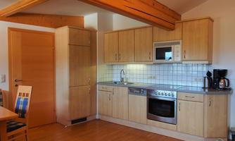 A modern kitchen with bright wooden furniture and a functional setup. On the countertop, there is a stove, a microwave, and a coffee machine.