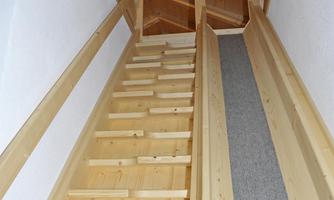 A bright wooden staircase leads upwards. The walls are plain and the stairs have a soft carpet on the side.