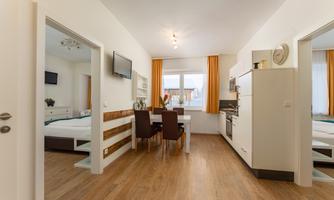 A modern room with a dining table and two chairs. The kitchen is equipped and the large windows let in plenty of light.