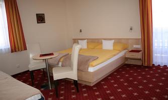A cozy hotel room with a double bed, a table, and chairs. The walls are painted in light colors and there are large windows with curtains.
