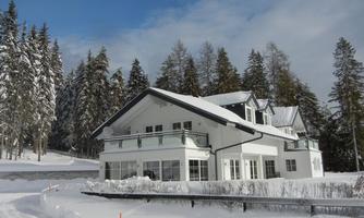 A modern house in a snow-covered landscape. Surrounded by tall, green trees and a clear sky.