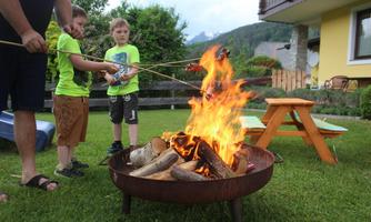 A family barbecue evening outdoors. Two children are roasting sausages over a fire in a garden.